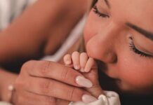 Czy poród naturalny zawsze jest lepszy dla psychiki mamy i dziecka Mama czule całuje dłoń noworodka trzymaną w swoich rękach