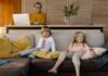 Starsza kobieta pracuje zdalnie na laptopie, wnuki bawią się na kanapie